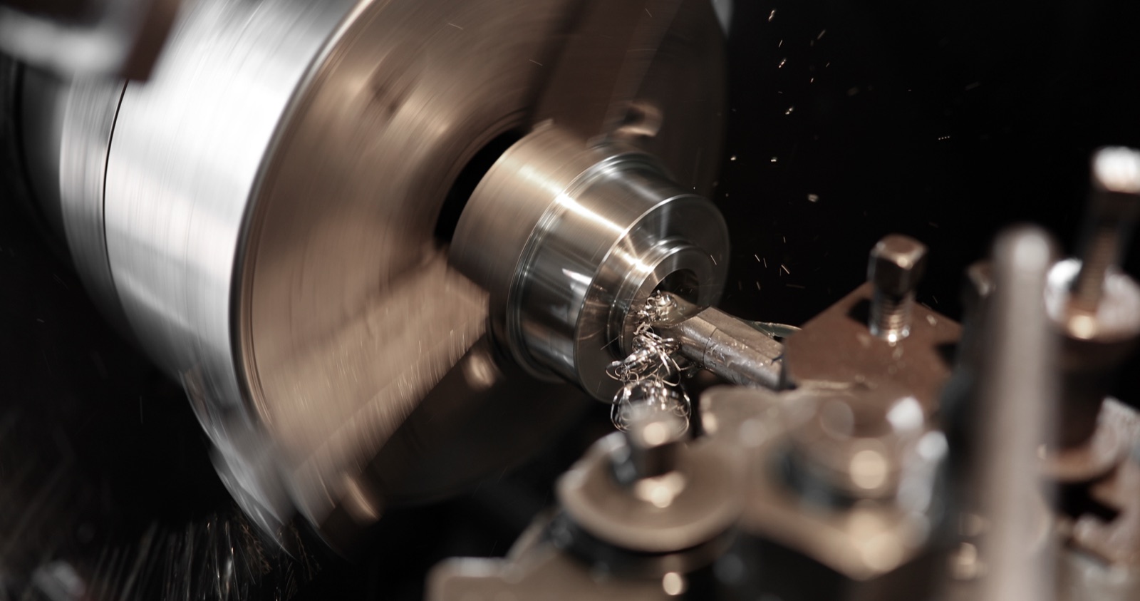 Macro shot of a CNC lathe turning a metal part, with metal shavings curling off the cutting edge.