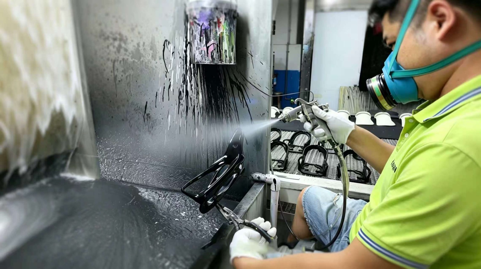 A Fudakin painter spraying a bottle cage inside the spray booth, with masked parts on the line behind.