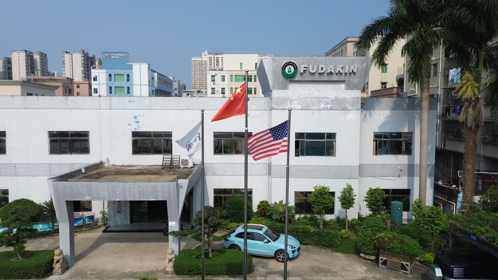 The front of the white two-story Fudakin headquarters building in Shenzhen, with the FUDAKIN sign on the roofline and three flagpoles out front.